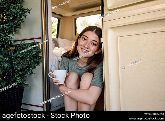 Beautiful woman holding coffee cup sitting at camper doorway