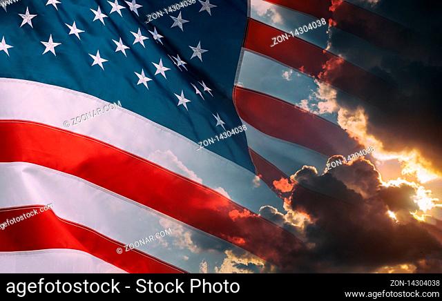 Cloudy sky and bright sunrise over the horizon of American flag waving in the wind