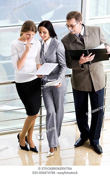 Smiling Hispanic businesswoman giving advices to her colleague and curious businessman in eyeglasses with opened paper case in his hands
