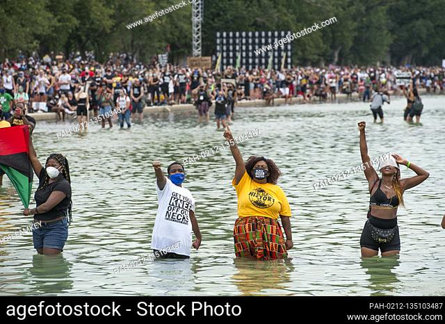 People stand in the cool water of the Reflecting Pool and raise their fists, during the “Get Your Knee Off Our Necks” March on Washington at the Lincoln...