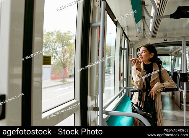 Woman with electric push scooter looking away while talking on mobile phone in tram