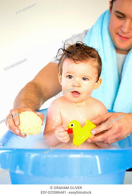 Young father bathing his son. He is holding a rubber duck and a sponge