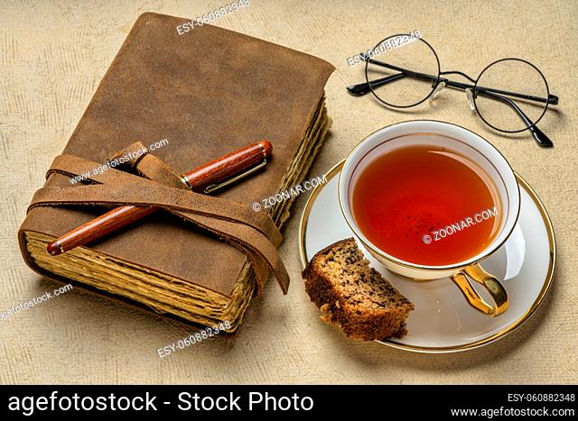 antique leather-bound journal with decked edge handmade paper pages and a stylish pen, a cup of tea and piece of banana bread, journaling concept