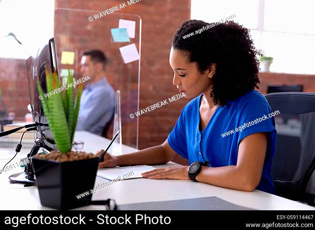 Busy african american businesswoman sitting at desk with hygiene screen writing in office