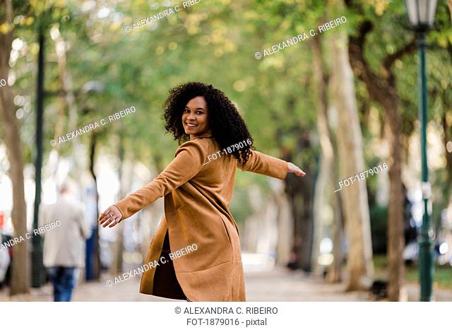 Portrait carefree young woman dancing on treelined sidewalk