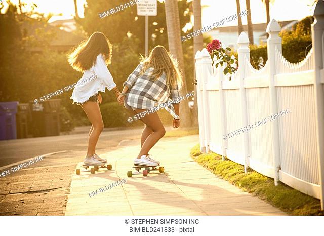 Teenage girls skateboarding on sidewalk