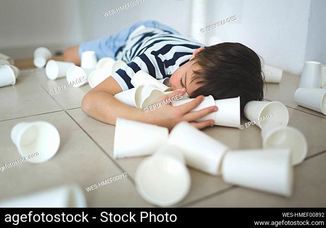Little boy lying on the floor between white paper cups