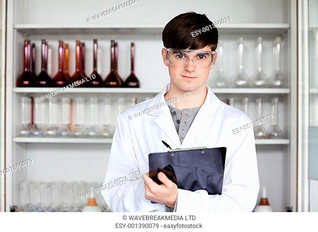 Male science student writing on a clipboard in a laboratory