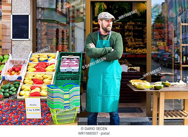 Grocer with arms crossed in front of greengrocer's shop
