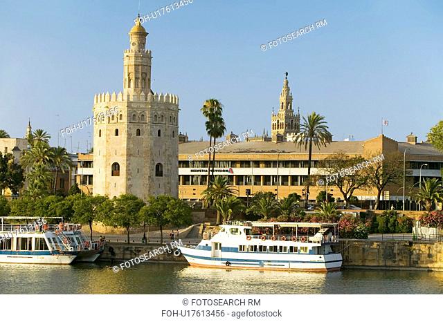 View of the tour boats and octagonal tower of Torre del Oro makes golden reflection on Canal de Alfonso of Rio Guadalquivir River, Sevilla Spain