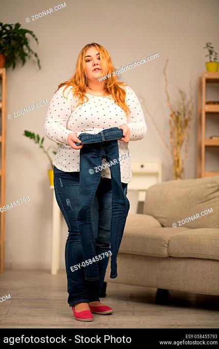 Plumb woman holding small size jeans in hand. Weight loss concept
