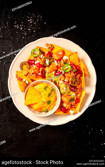 Nachos with beef, guacamole and cheese sauce, top shot on a black background with a place for text