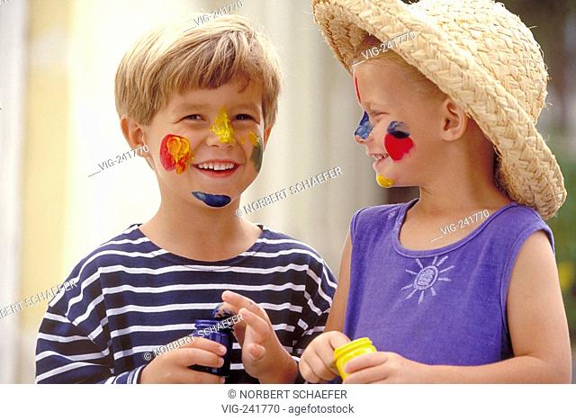 portrait, close-up, boy and girl wearing strawhat, both 6 years old wearing blue shirts painting each others face with finger paints  - GERMANY, 08/08/2004