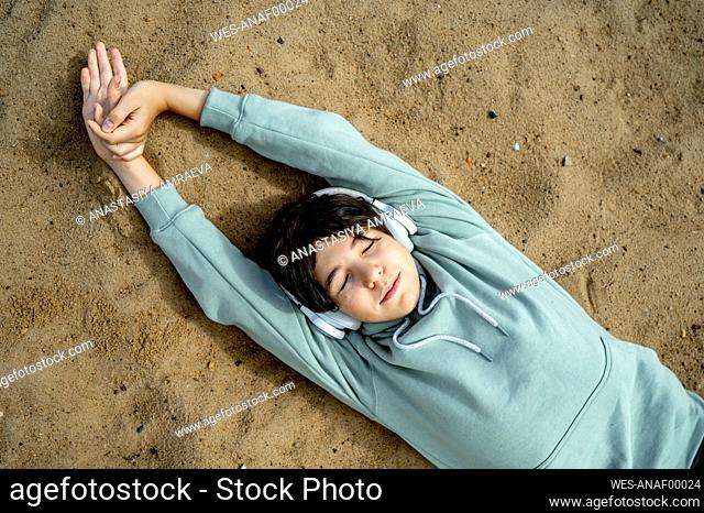Boy wearing wireless headphones relaxing on sand at beach