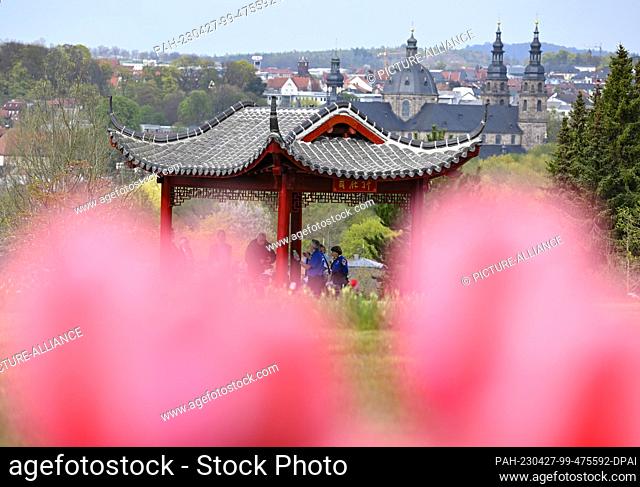 27 April 2023, Hesse, Fulda: Fulda Cathedral can be seen behind blooming tulips and a Chinese temple in the State Garden Show's cultural garden