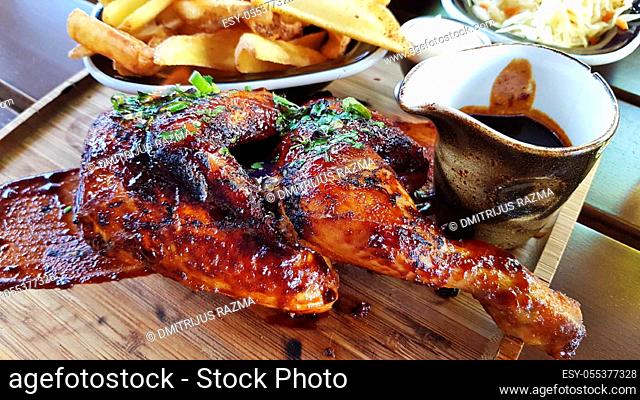 Half of the fried chicken is served on a wooden tray. On a tray fried potatoes and sauce. Finely chopped green onions on fried chicken