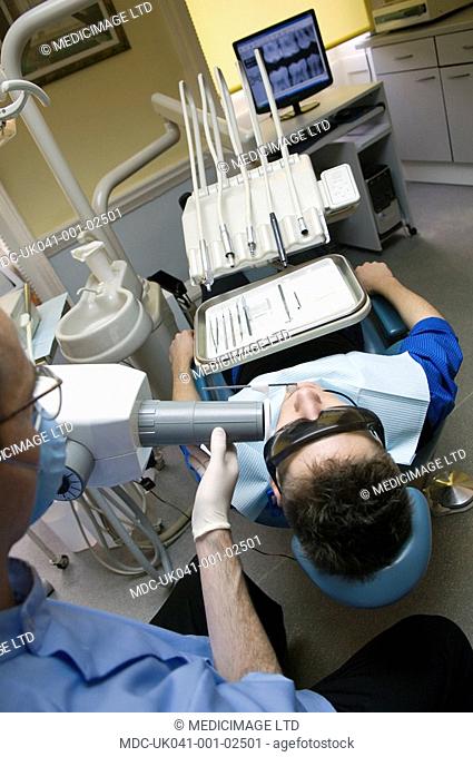Dentist wearing safety glasses and mouth mask xrays the teeth of young male patient, also wearing special protection glasses
