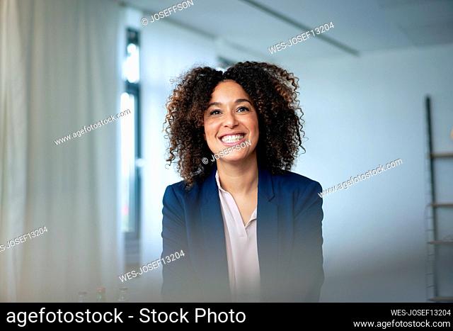 Happy businesswoman with curly hair clenching teeth at workplace