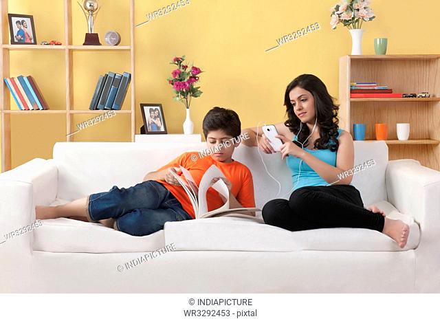 Sister sitting on couch listening to music while her brother looking at phone