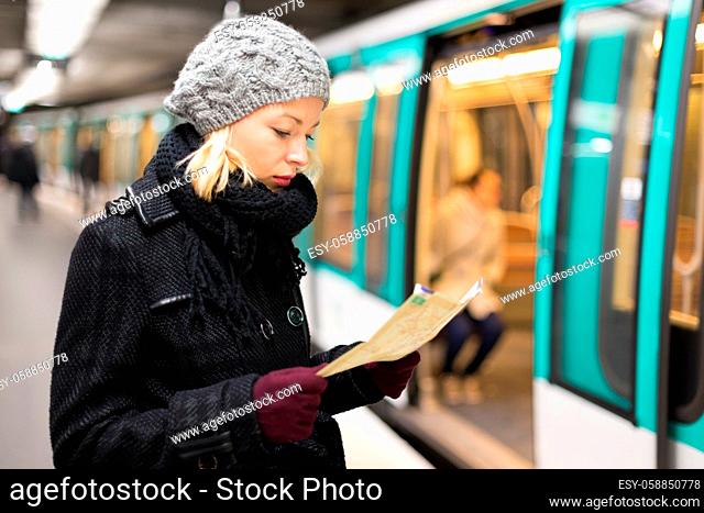 Casually dressed woman wearing winter coat, waiting on a platform for a train to arrive, orientating herself with public transport map