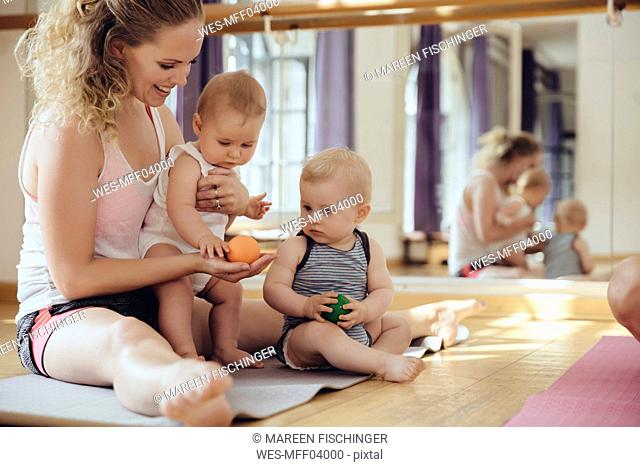 Mother with playing twin babies sitting on yoga mat