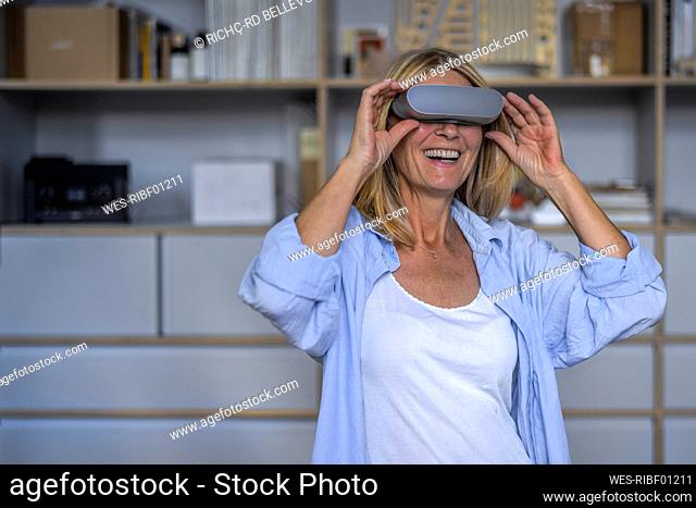 Happy mature woman wearing virtual reality glasses at home