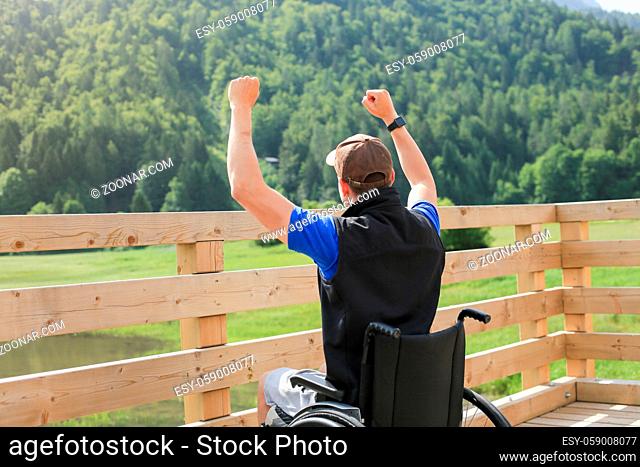Disabled young man on a wheelchair in nature feeling excited and full of optimism like a winner