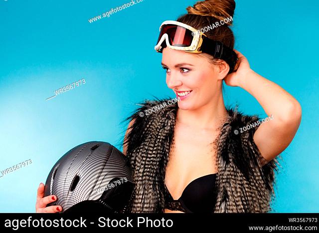 Woman sexy hot skier girl wearing black bra fur vest ski googles holding helmet. Winter sport activity. Beautiful seductive sportswoman on blue studio shot
