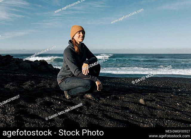 Smiling woman crouching on sand at Janubio Beach, Lanzarote, Canary Islands, Spain