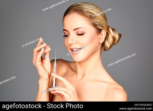 beautiful happy young woman holding syringe with collagen treatment injection. beauty shot on grey background. copy space