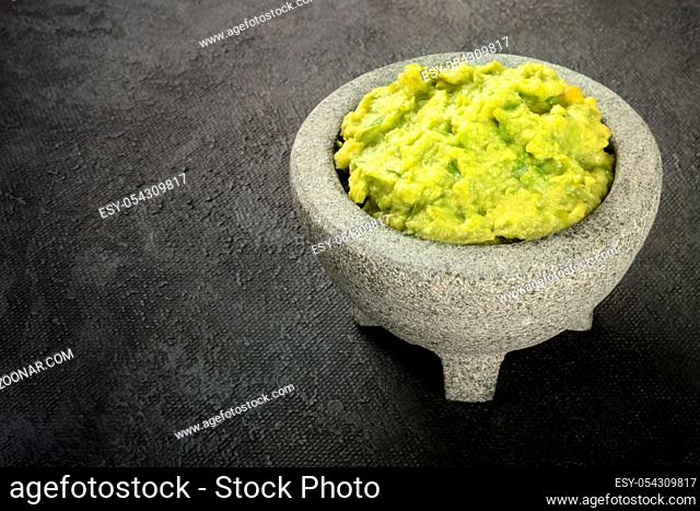 Guacamole in a molcajete, Mexican avocado dip sauce in the traditional stone mortar, on a black background with copy space