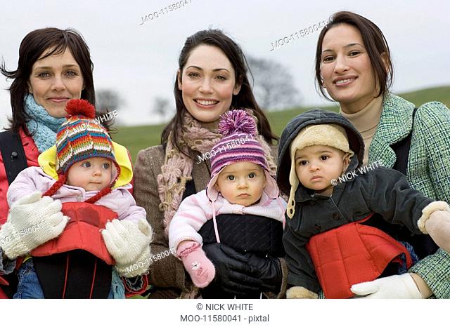 Two mothers with babies in baby carriers in park