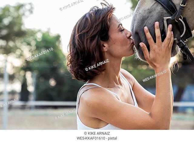 Woman kissing nustrils of riding horse