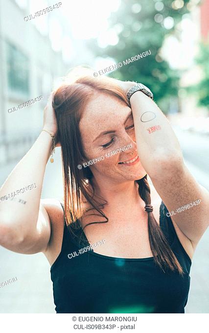 Young woman with long red hair and freckles with eyes closed on city street