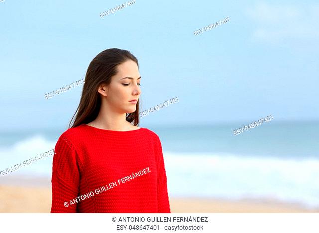 Melancholic woman in red walking alone on the beach