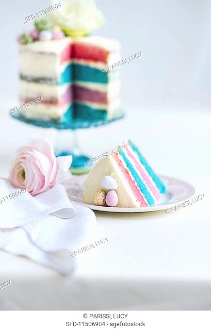 A four-layer rainbow cake with white icing, Easter eggs and flowers (sliced)