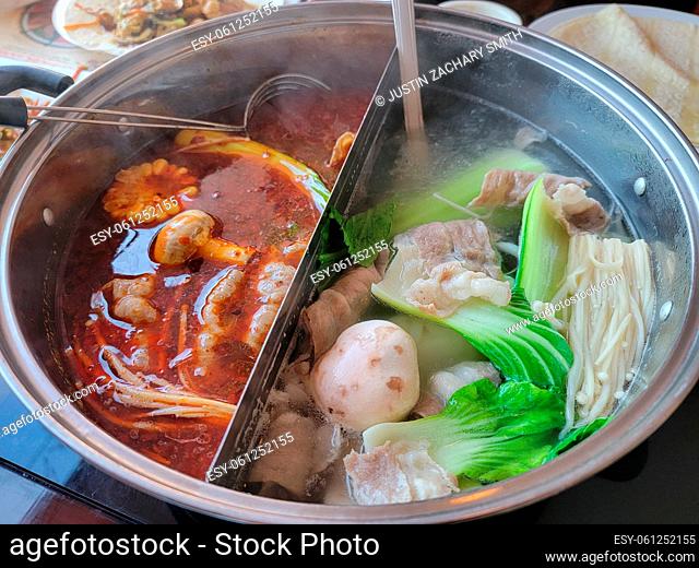 Chinese or asian hot pot with spicy and regular broth and meat and vegetables and spoons