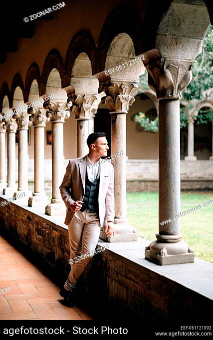 Groom in a suit stands leaning on the windowsill of a loggia with columns in an old building on Lake Como. High quality photo