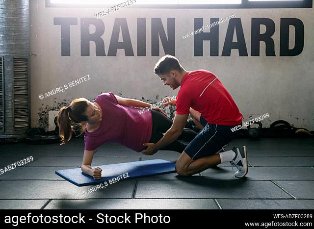 Fitness instructor assisting female athlete in practicing plank position on mat at gym