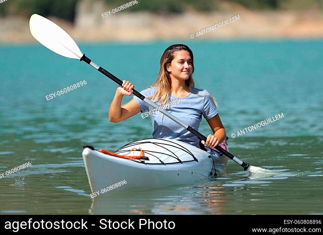 Happy woman rowing in kayak looking at side in a lake on summer vacation