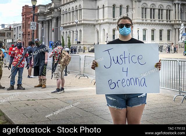 Peaceful protester holds signage demand of ""Justice 4 Breonna"" in front of armed and masked protesters at the area of Friday night’s rioting on May 30