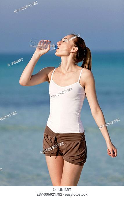 Girl young woman refreshing drinks water from a bottle on the beach by the sea in summer vacation