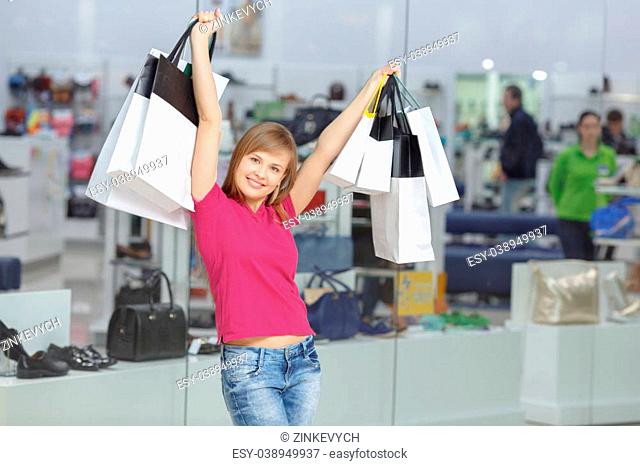 Wow shopping. Young cheerful girl in casual clothes raises her hands with shopping bags
