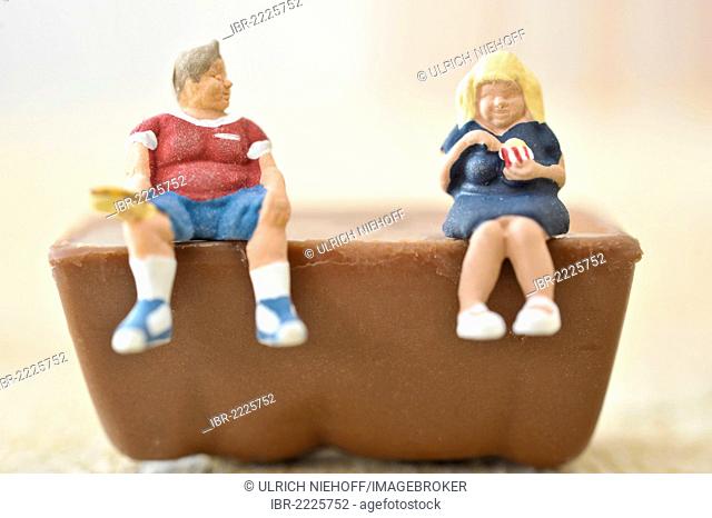 Miniature obese figures sitting a piece of chocolate