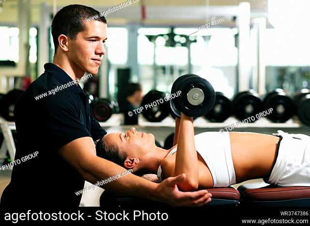Woman with her personal fitness trainer in the gym exercising on bench with dumbbells