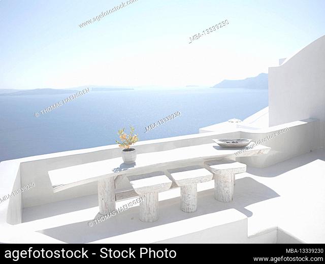Scenic view of a white balcony with a flower in Oia on Santorini island with traditional cycladic, white houses and churches with blue domes over the Caldera
