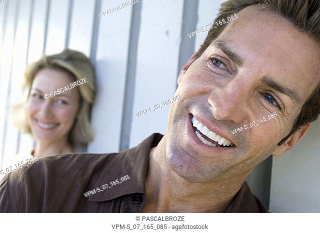 Close-up of a mid adult man smiling with a mid adult woman standing behind him
