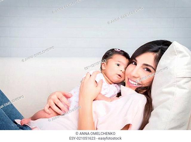 Happy mother with baby lying down on the couch at home, cheerful woman playing with her adorable daughter, love and happiness concept