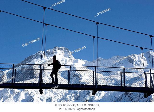 Hiker at swingbridge in snow covered Mountains