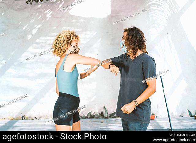 Man and woman wearing mask giving elbow bump while standing against wall